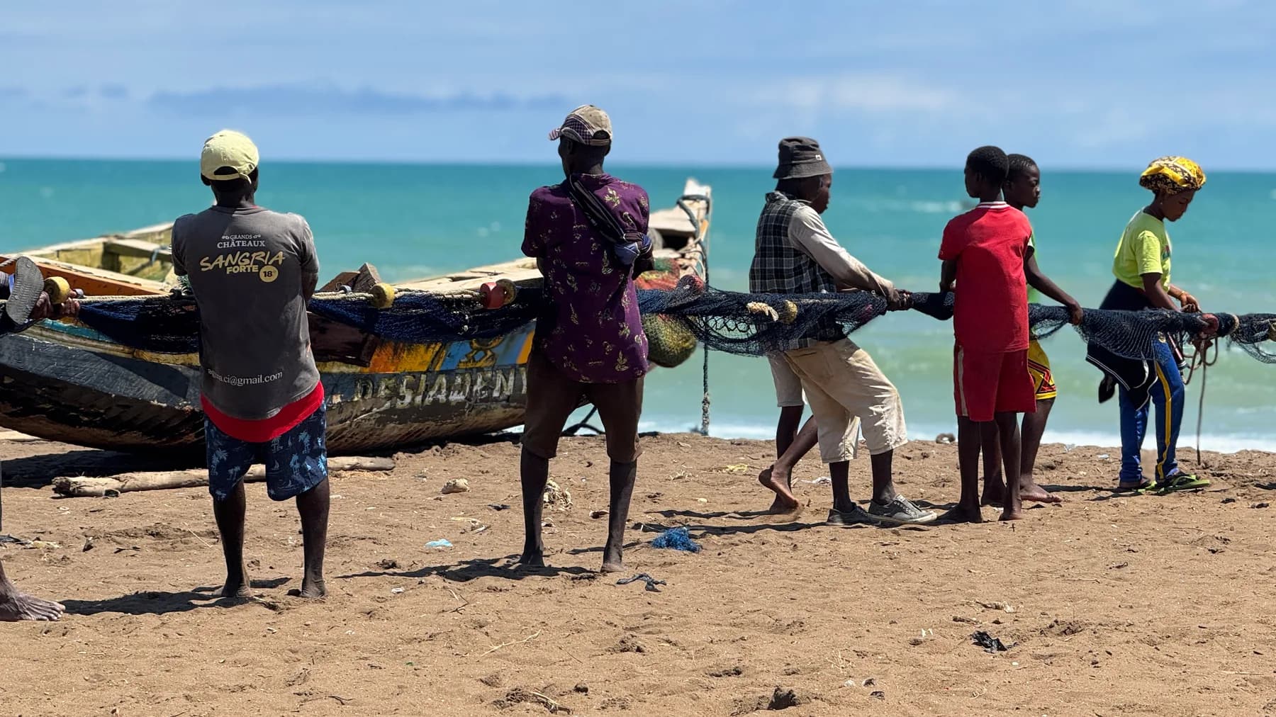 Fishing community pulling a net beside boats on the coast of Togo